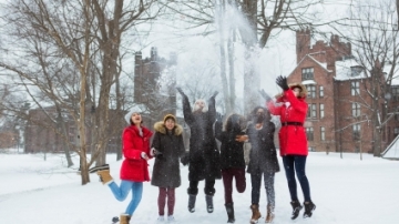 A group of alums who threw snow in the air and are jumping up dressed in winter garb.