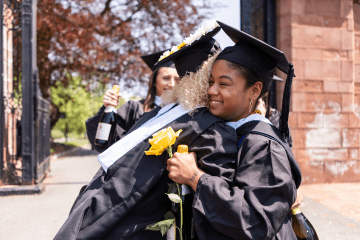 Two graduates hugging while wearing their graduation robes and caps