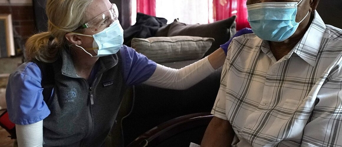 Alum Dr. Megan Young, left, offers support to Edouard Joseph, 91, moments after giving him a COVID-19 vaccination, Thursday, Feb. 11, 2021, at his home in the Mattapan neighborhood of Boston. (Photo courtesy of AP)