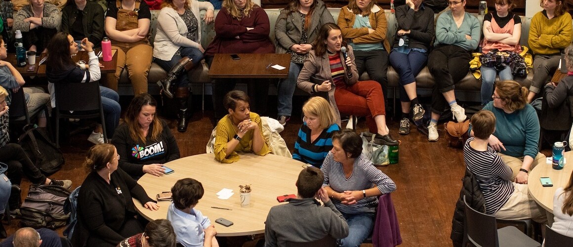 Aerial view of audience sitting at tables in conversation, BOOM panel.