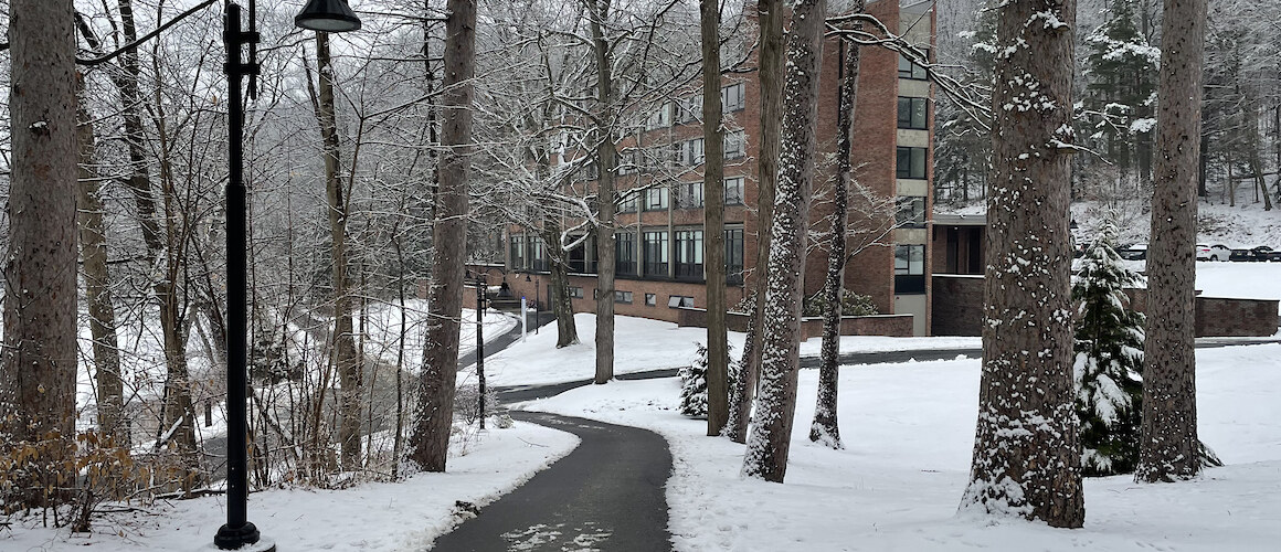 An empty, plowed path on campus on a snowy day. A residence hall can be seen in the distance.