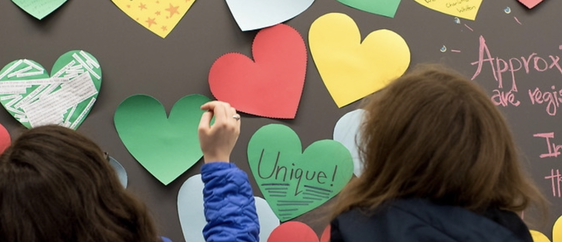 Students standing at a blackboard covered with stickynote hearts containing messages about disability