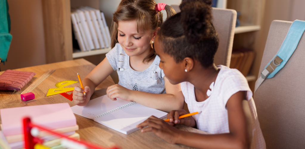 Two students looking at a blank notebook with math paraphernalia around them on the desk.
