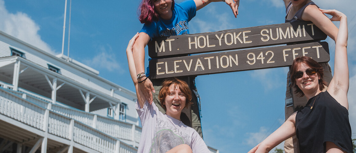 Students making a heart shape with their arms around the Mt. Holyoke state park sign. Mountain Day 2024. Photo by Max Wilhelm.