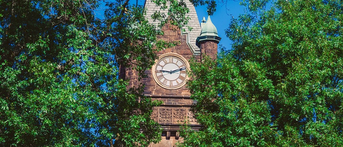 Mount Holyoke College's Clocktower slightly obscured by green leaves with a bright blue sky.