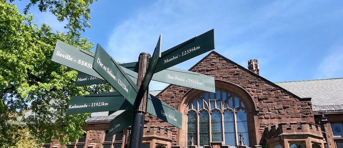 Directional sign on campus pointing to various international cities and their distance from campus.