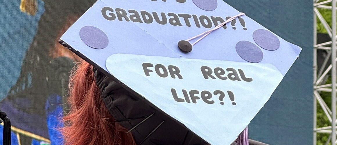 A 2024 graduate of Mount Holyoke College wearing a mortarboard decorated with the phrase “It’s graduation?! For real life?!”