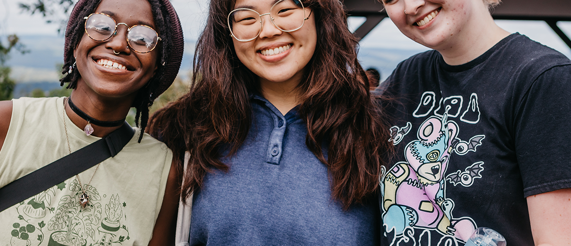 Three students smiling widely on the top of Mount Holyoke on Mountain Day 2022