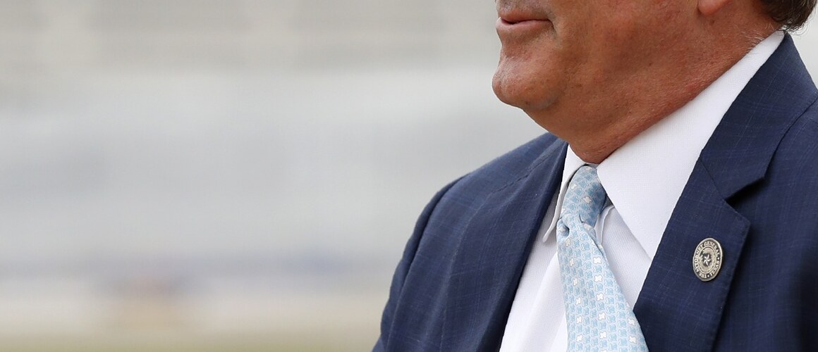 Ken Paxton, balding, waiting on a tarmac, tie flapping in the wind, gesturing