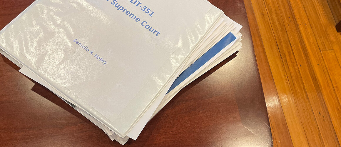 A white binder with a title page that reads "POLIT-351 The Supreme Court Danielle R. Holley" on a wooden table.