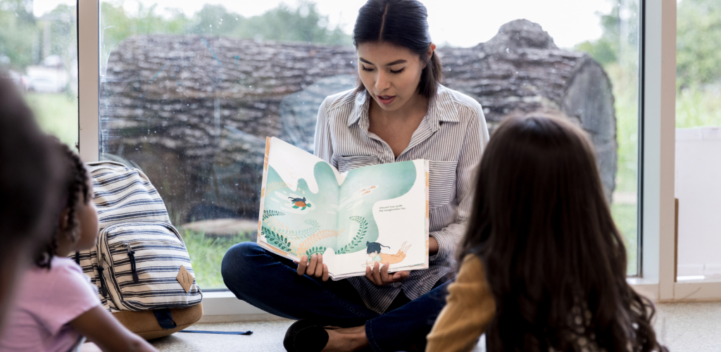 Woman reading book to students. Stock photo courtesy Canva.