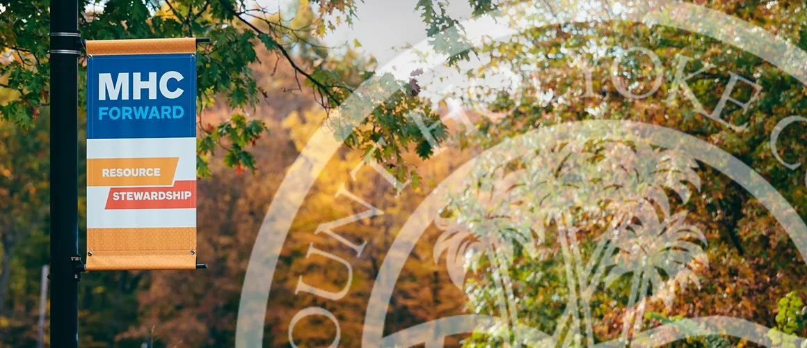 A lamp post banner on the Mount Holyoke campus promoting the Resource Stewardship pillar of the MHC Forward strategic plan, with MHC logo watermarked over it.